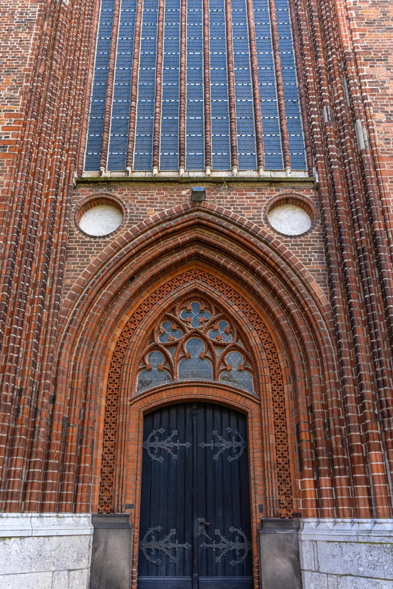 어두운 문이 있는 붉은 벽돌 바실리카의 극적인 고딕 정면