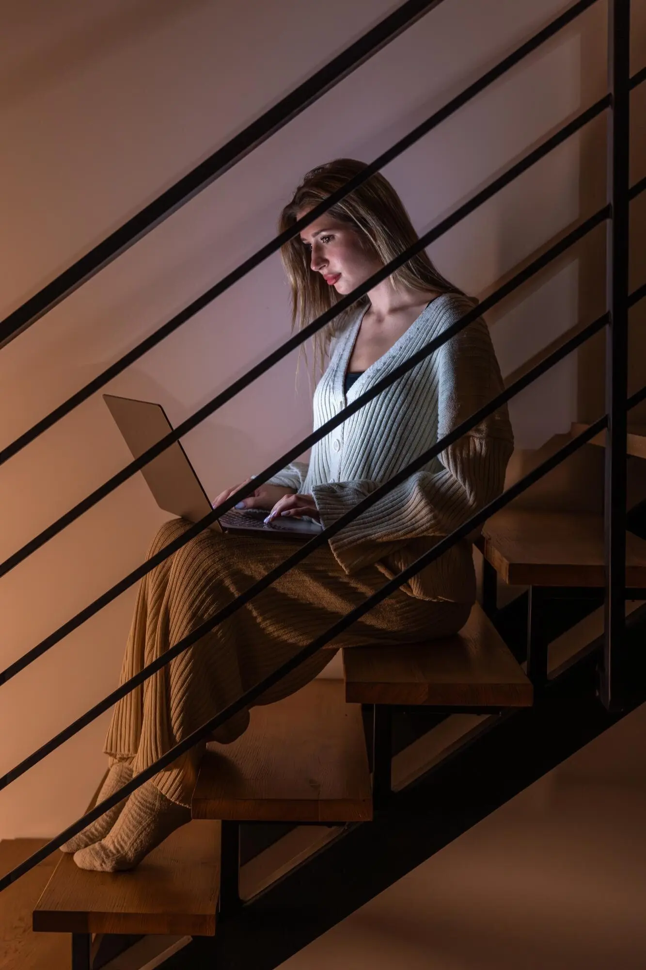 아늑한 저녁의 집 안 계단에서 노트북으로 밤에 일하는 젊은 여성